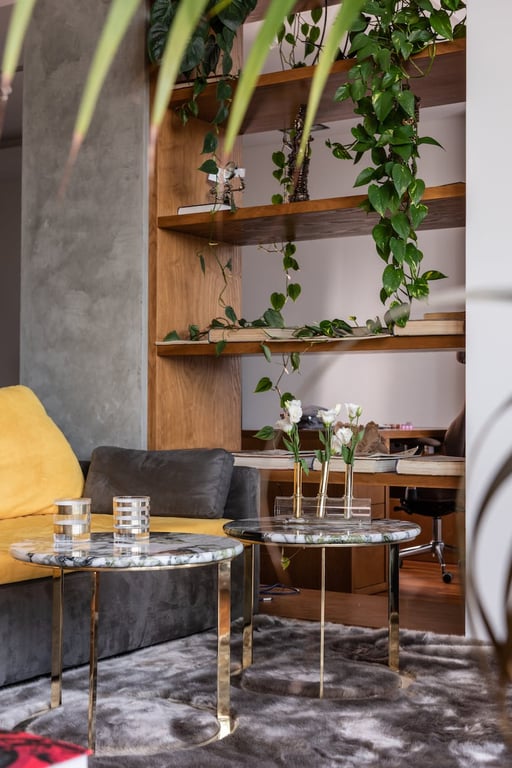 Détails intérieurs d'un appartement moderne avec des tables en marbre placées près d'un canapé confortable et des étagères en bois décorées de plantes fraîches.